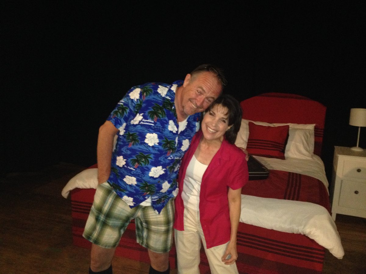 Mark Whelan in a Hawaiian shirt with a fellow actor on a bedroom set