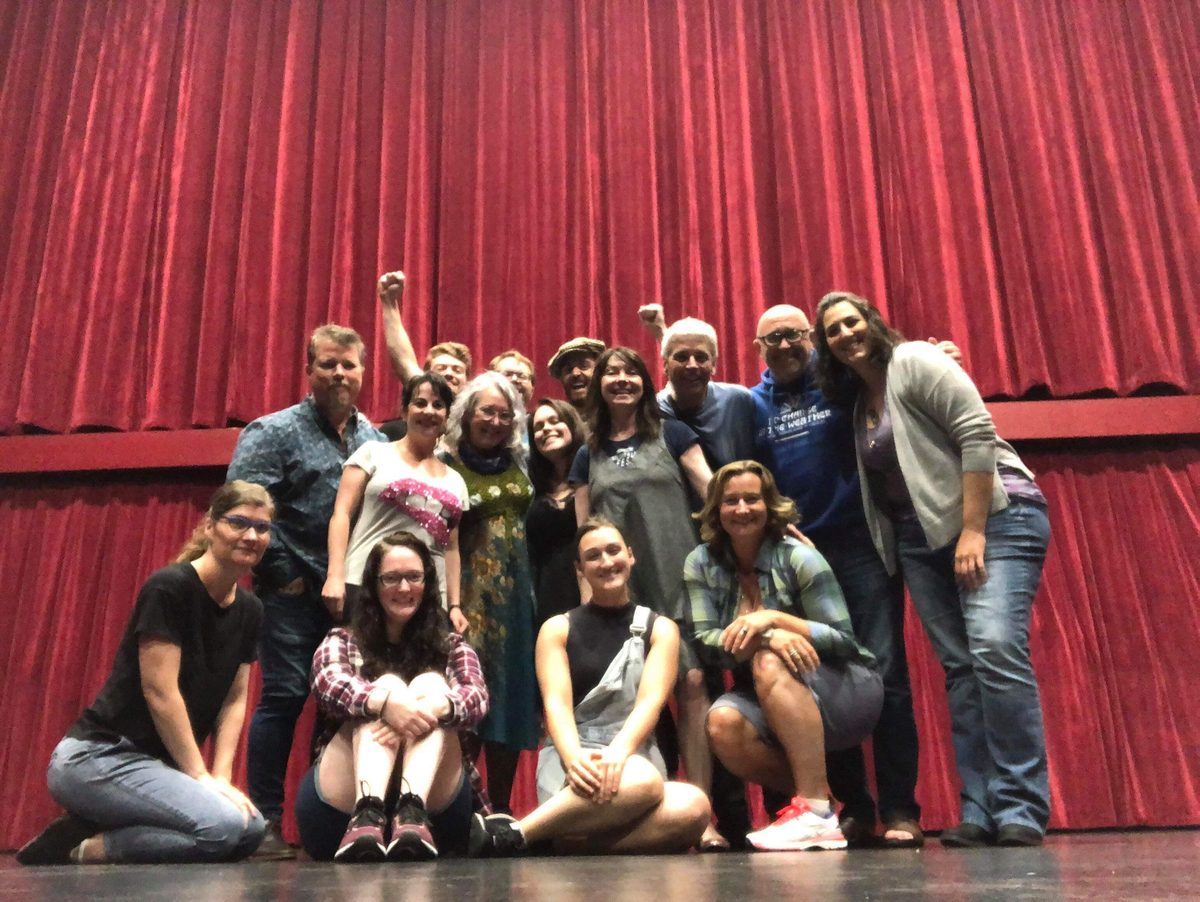 Cast and crew photo in front of a red stage curtain