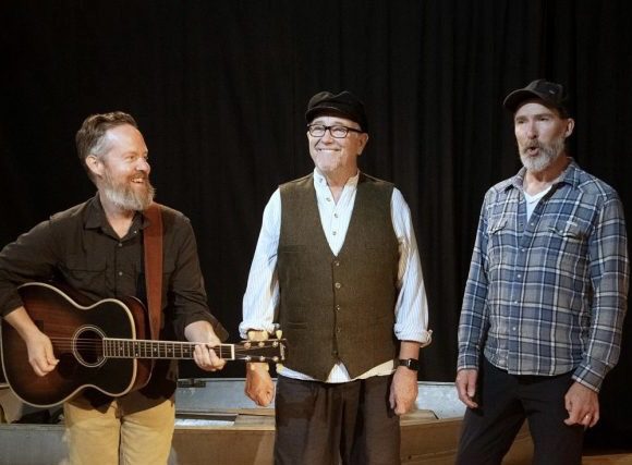 Mark Whelan on stage between a guitarist and another actor