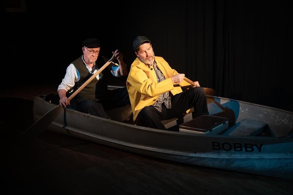 Mark Whelan rowing a small boat on stage with another actor