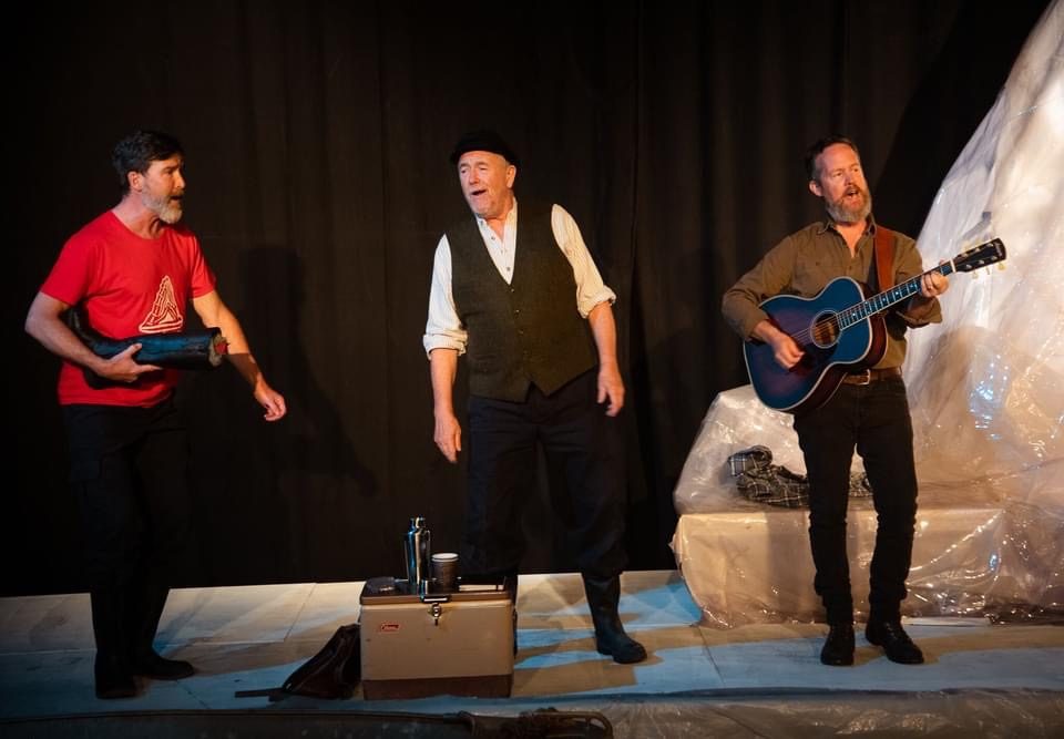 Mark Whelan singing on stage between two musicians